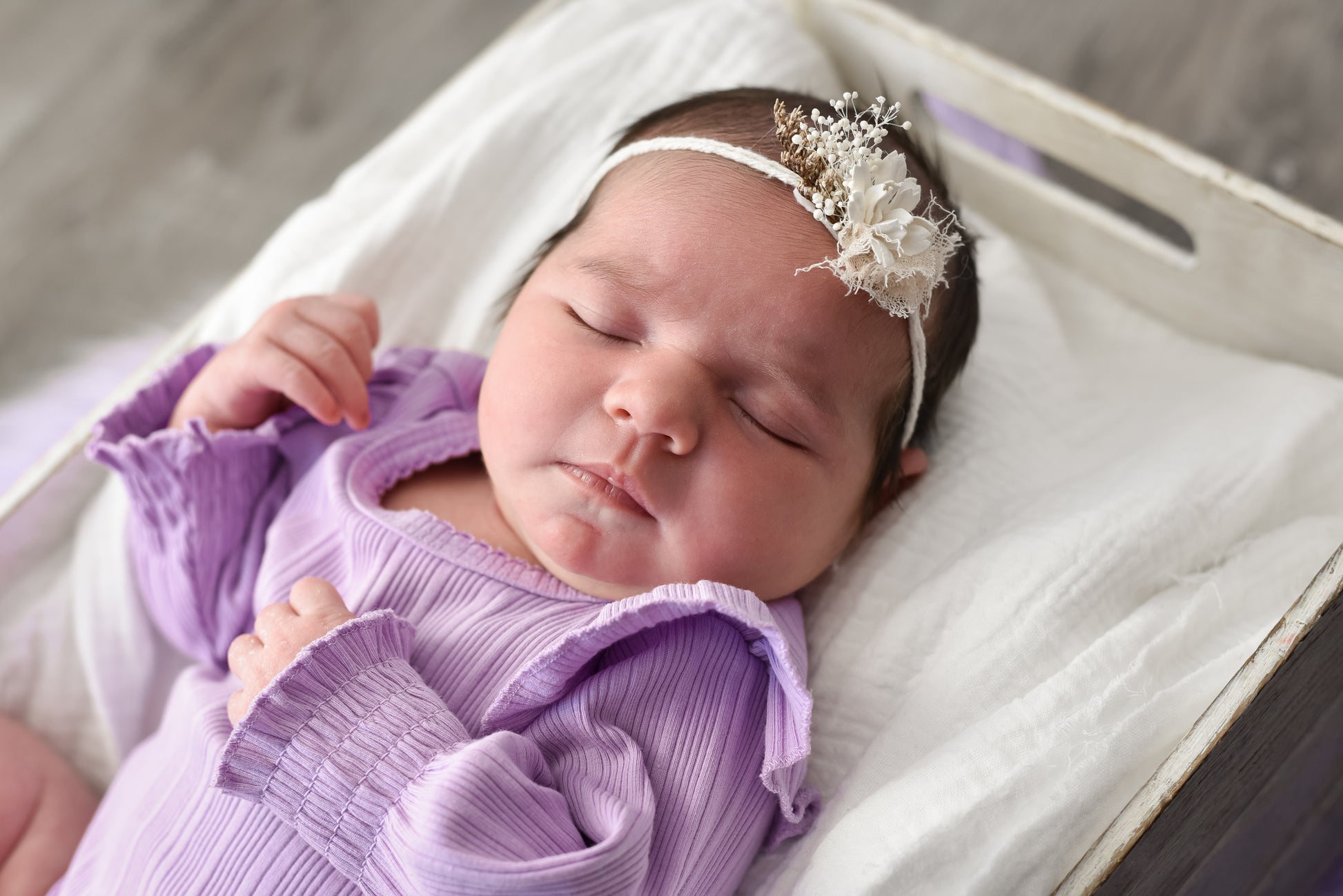 Newborn baby wearing a purple outfit and white headband with flowers.